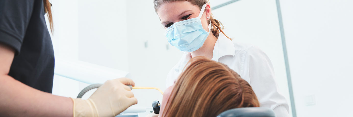 Nahaufnahme einer Patientin auf dem Behandlungsstuhl, während sie von der Zahnärztin und der Assistentin behandelt wird